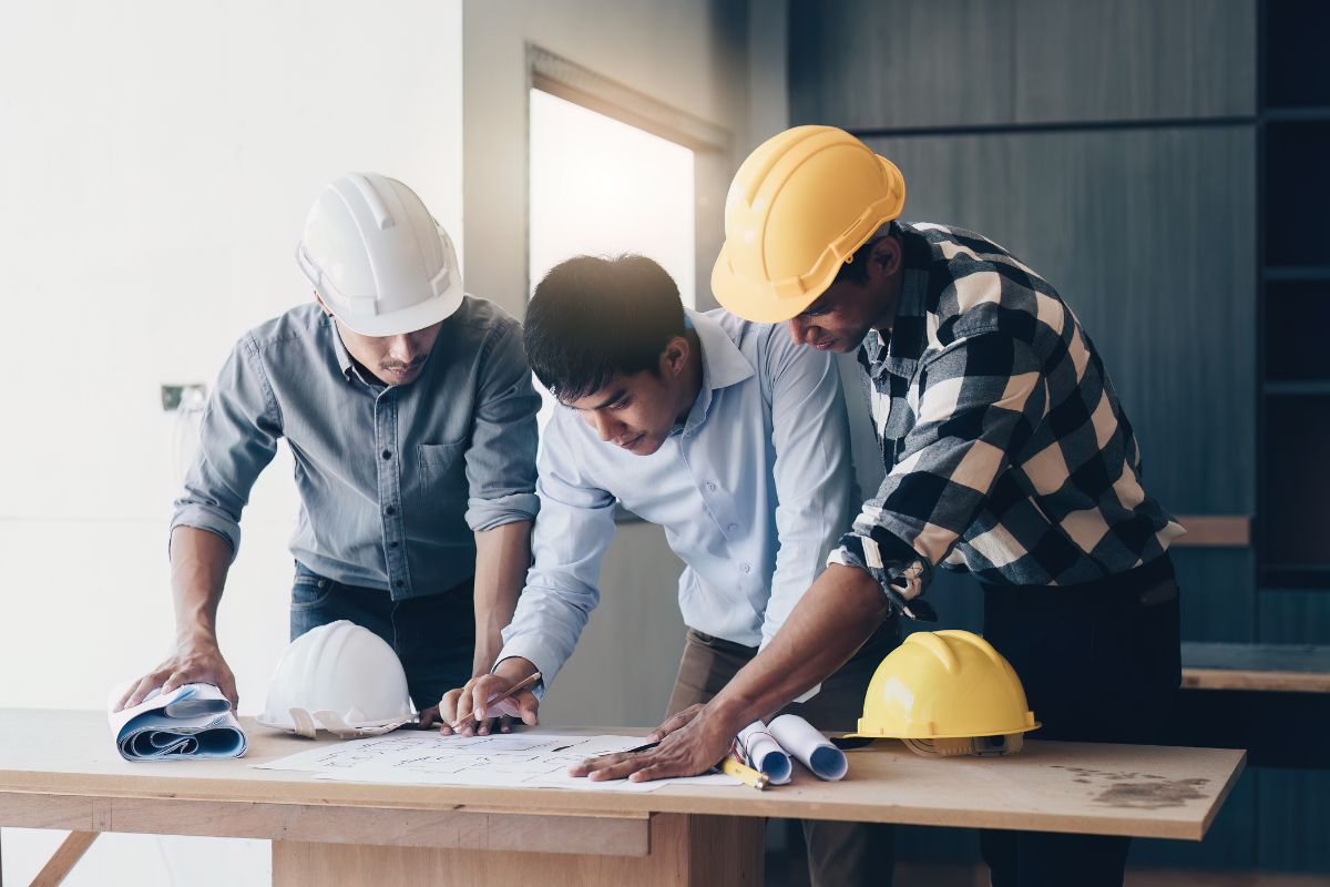 3 people in hard hats look at architectural drawings on a table